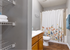 Bright and inviting bathroom with elegant floral shower curtain, ample wooden cabinetry, and sleek shelving for optimal storage.