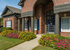 Charming brick apartment exterior with classic columns, vibrant flower beds, and inviting front entrance.