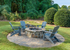 Charming outdoor stone fire pit area with Adirondack chairs surrounded by lush greenery for a relaxing retreat.