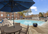 Inviting apartment complex with a sparkling pool, lounge chairs, and shaded seating area under a large umbrella, perfect for relaxation and enjoyment.
