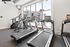 State-of-the-art fitness center with modern treadmills and elliptical machines, overlooking a scenic view of a luxurious apartment complex and pool.