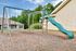 Charming outdoor playground with swings and slide, surrounded by lush greenery in a family-friendly community setting.