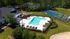 Inviting aerial view of a luxury apartment community featuring a shimmering outdoor pool with ample lounge seating, adjacent to a recreational area, all set against a backdrop of lush greenery.
