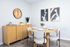 Stylish dining area featuring a round table set with elegant dinnerware, cozy cushioned chairs, minimalist decor with modern art, and a striking wall clock.