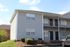 Charming two-story apartment building with modern gray siding, front balconies, and a well-maintained garden, featuring ample parking space on a sunny day.
