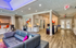 Modern apartment lounge showcasing elegant hardwood floors, vibrant art pieces, and stylish seating. Features include a cozy gray sofa, open desk area with barstools, and inviting ambient lighting.