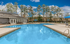 Inviting outdoor pool area with pristine blue water, surrounded by lounge chairs and shaded by vibrant umbrellas, nestled next to a modern clubhouse and lush green trees.