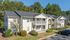 Charming two-story apartment building with balconies, surrounded by lush greenery and ample parking space, offering a serene and inviting living environment.