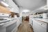 Bright, modern kitchen with white cabinetry and sleek appliances leading to a cozy dining area with warm wood flooring.