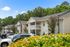 Charming suburban apartment complex with modern balconies, lush greenery, and ample parking beneath a clear blue sky.
