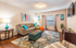 Inviting living room with modern decor, vibrant artwork, cozy gray sofa, and abundant natural light.