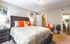 Inviting bedroom with modern decor, featuring vibrant orange accents, a plush bed, and a cozy seating area.