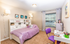 Charming bedroom with a cozy lavender bedspread, stylish desk with colorful decor, and ample natural light through large windows.