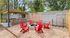Inviting outdoor space featuring a cozy fire pit surrounded by vibrant red chairs and a rustic stone barbecue area, perfect for entertaining.