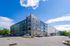 Modern four-story apartment building with sleek design, ample parking, and lush green surroundings under a vibrant blue sky.