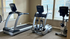 Modern gym room with state-of-the-art treadmill, elliptical, and stationary bike, filled with natural light from large windows.