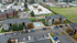 Aerial view of a charming apartment complex with two-story buildings, vibrant landscaping, and a centrally located swimming pool, set against a backdrop of open green fields.