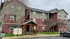 Charming apartment complex with vibrant red and tan exterior, surrounded by lush greenery and featuring convenient bicycle parking.