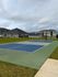 Inviting outdoor sports court with vibrant blue and green surfaces, surrounded by lush green grass and modern residential buildings under a cloudy sky.
