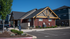 Charming community office with rustic architecture, surrounded by well-maintained greenery and ample parking, under a clear blue sky.