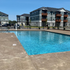 Inviting apartment community pool with crystal-clear water, surrounded by modern three-story buildings under a bright blue sky.