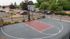 Modern outdoor basketball court with sleek design, surrounded by greenery and parking, perfect for community sports.