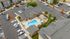 Aerial view of a modern apartment complex featuring a central swimming pool, surrounded by well-maintained landscaping and ample parking spaces.