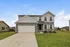 Charming two-story home with elegant stone facade, spacious driveway, and lush green lawn, set against a clear blue sky.