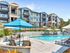 Luxurious apartment complex with modern balconies, a sparkling outdoor pool, and vibrant landscaping under a clear blue sky.