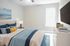 Bright, cozy bedroom with elegant decor, soft blue and white tones, plush bedding, modern furniture, and a large wall-mounted TV.
