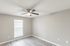 Bright, empty room with modern ceiling fan and large window, featuring sleek laminate flooring and soft gray walls.