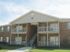 Charming two-story apartment building with brick exterior and well-maintained balconies, surrounded by lush greenery and a clear sky.