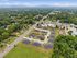 Scenic aerial view of a peaceful residential community with well-maintained roads, lush greenery, and comfortably spaced homes under a clear blue sky.
