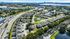 Aerial view of a picturesque residential neighborhood with modern villas, lush green landscaping, and a central swimming pool, nestled near scenic waterways and vibrant cityscape.