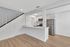 Modern apartment kitchen with sleek stainless steel appliances, elegant white cabinetry, and stylish wood flooring beneath an airy staircase.