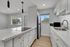 Bright and modern kitchen with sleek white cabinetry, elegant countertops, and stainless steel appliances, complemented by stylish pendant lighting and a scenic window view.