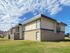 Contemporary apartment complex with sleek design, surrounded by lush green lawns and a clear blue sky.