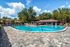 Blue curved pool with brick walkway surrounding. Lounge chairs and umbrellas in the background
