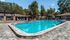 Blue curved pool with brick walkway surrounding. Lounge chairs and umbrellas in the background