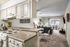 Kitchen with beige cabinets, stainless steel sink, white stove, lights under cabinets and a passthrough to the living room.
