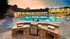 Community pool surrounded by lounge chairs. Gas grill encased in stone counter in foreground.