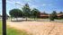 Beach volleyball pit surrounded by green grass, trees and apartment building in background.
