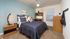 Bedroom with window, teal accent wall, end table, bed, ceiling fan, study desk and drawers.