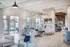 Resident lounge with large windows, chairs and couches, and a wall mounted television and fireplace.