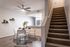 Apartment living and dining area with kitchen in the background, and staircase leading upstairs to the right. The dining set is circular with a white table and chair.