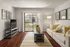Living room room with wood style flooring, TV, coffee table, and cream colored couch. Sliding glass door overlooks grass exterior.