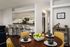 Dining area with wooden table and yellow chairs. Kitchen and breakfast bar visible in the background.