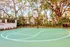 Full size basketball court with fenced in with trees surrounding it.  Tennis court in background..