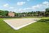 Beach volleyball pit surrounded by green grass, trees and apartment building in background.