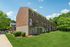 Two floor brick apartment building with trees in background.